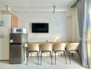 Una cocina moderna con una mesa de comedor, sillas, un refrigerador, un microondas y un televisor de pantalla plana montado en la pared.