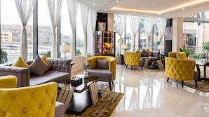 A spacious living area with modern furnishings, large windows, and a view of the cityscape. - Gardn Millennium Hotel Abha (Abha)