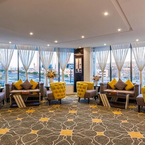 A hotel lobby with a modern design, featuring sofas and armchairs arranged around a central coffee table, large windows with curtains, and a patterned carpet. - Gardn Millennium Hotel Abha (Abha)