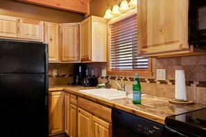A kitchen with wooden cabinets, a black refrigerator, a coffee maker, a toaster, and a dishwasher. - Spacious Adventure Cabin with Direct Trail Access near Island Park, Idaho (Island Park)