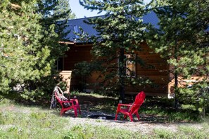 A cabin with a wooden exterior, surrounded by trees, and two red chairs in front. - Spacious Adventure Cabin with Direct Trail Access near Island Park, Idaho (Island Park)