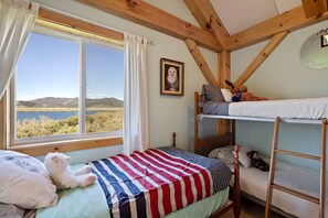 A room with a bunk bed, a single bed with an American flag bedspread, a window with a view of a lake and hills, and a wooden ladder. - Rustic Lakefront Cabin with Private Oasis near Henrys Lake, Island Park, Idaho (Island Park)