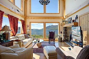 A spacious living room with a large window offering a scenic view of a lake and mountains. - Rustic Lakefront Cabin with Private Oasis near Henrys Lake, Island Park, Idaho (Island Park)