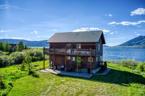 Een houten chalet met twee verdiepingen en een balkon, aan een meer gelegen met bergen op de achtergrond.