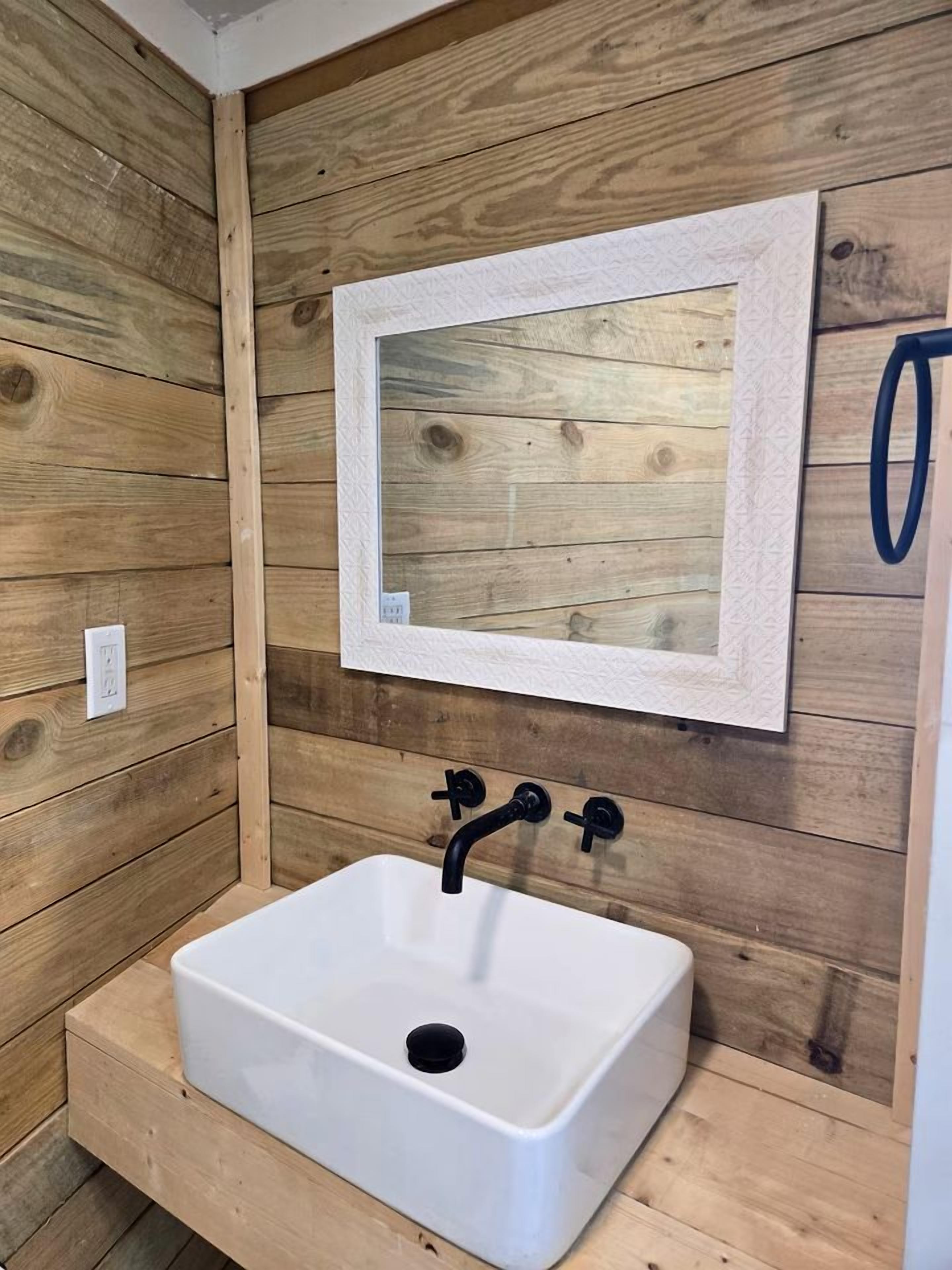 A bathroom with a white sink, wooden walls, and a framed mirror.