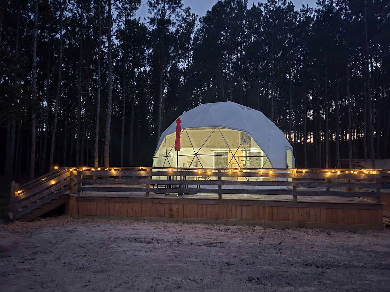 A dome-shaped structure with a wooden deck and railing, surrounded by trees.