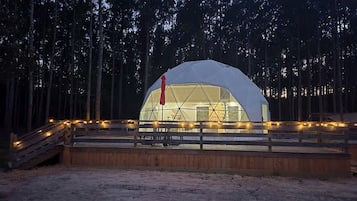 A dome-shaped structure with a wooden deck and railing, surrounded by trees.