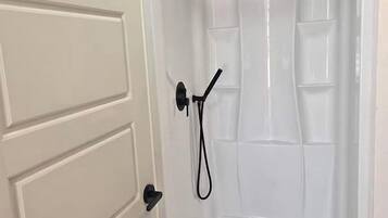 A white door with a black handle, leading to a shower area with a transparent door and a showerhead.