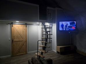 Una habitación con puerta de madera, una escalera de caracol y un televisor montado en la pared.