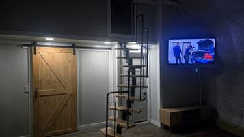 A room with a wooden door, a spiral staircase, and a television mounted on the wall.