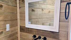 Une salle de bain avec un lavabo blanc, des murs en bois et un miroir encadré.