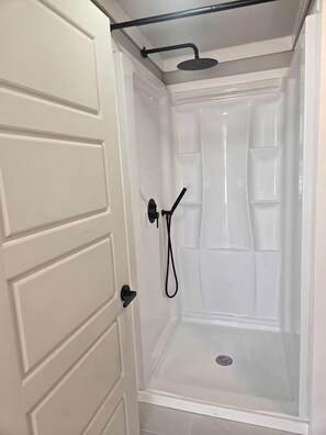 A white door with a black handle, leading to a shower area with a transparent door and a showerhead.