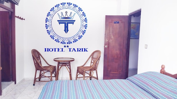 A hotel room with a bed, two wicker chairs, a small round table, and a wall-mounted emblem. - Hotel Tarik (Fnideq)