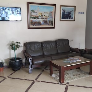 Sala de estar com sofá de couro, mesa de centro, planta em vaso e duas fotos emolduradas na parede.