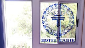 A room with a bed, a window with a logo, and a view of greenery outside. - Hotel Tarik (Fnideq)