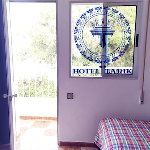 Quarto com cama, janela com logotipo e vista para área verde lá fora.