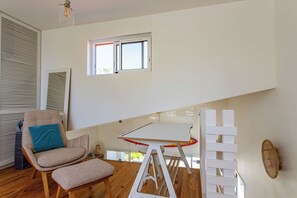 Ein Zimmer mit Holzboden, einem Stuhl mit Kissen, einem Tisch und einem Fenster mit Jalousien.