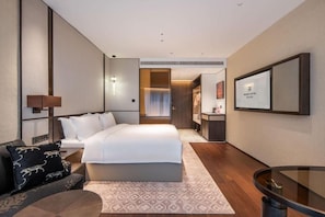 Habitación de hotel moderna con una cama grande, un escritorio, una silla, un sofá y una mesa de vidrio.