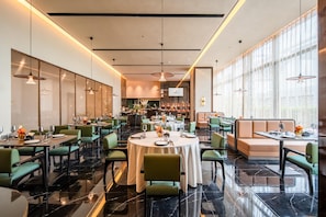 Un restaurante moderno con mesas redondas, sillas verdes y una zona de bar.