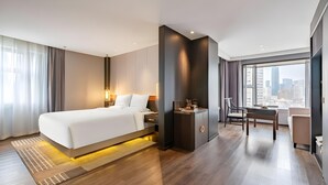 Moderni hotellihuone, jossa on suuri sänky, työpöytä ja näkymä kaupunkiin.