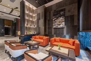 Een moderne lobby met een zithoek, een hanglamp en een groot abstract schilderij.