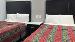 A room with two beds, each with a patterned bedspread and white pillows. There is a small black nightstand between the beds. - Studio6 Oakland, CA - San Francisco Berkeley Area (Oakland)