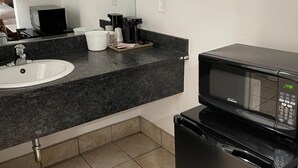 A hotel bathroom with a sink, countertop, mirror, and a black microwave. - Studio6 Oakland, CA - San Francisco Berkeley Area (Oakland)
