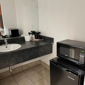A hotel bathroom with a sink, countertop, mirror, and a black microwave. - Studio6 Oakland, CA - San Francisco Berkeley Area (Oakland)