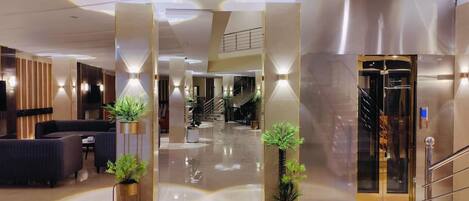 A modern hotel lobby with a central staircase, seating area, and a reception desk.
