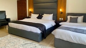 A hotel room with two beds, a wooden door, and a black armchair. - Pinemont Hotel Murree (Murree)