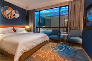 Camera d'albergo con un letto grande, due poltrone, un tavolino e vista su un paesaggio tropicale dalle finestre.