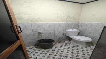 Un baño pequeño con un inodoro, un balde y paredes de azulejos.