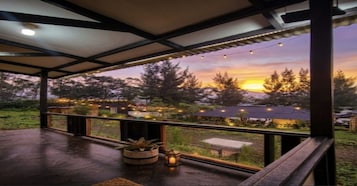 Una terraza al aire libre con vistas a la puesta de sol, barandilla y luces colgantes.