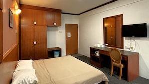 Ein Hotelzimmer mit einem Bett, einem Schreibtisch, einem Sessel, einem Fernseher und Holzschränken.