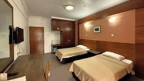 Ein Hotelzimmer mit einem hölzernen Kopfteil, zwei Einzelbetten, einem Holztisch, einem Fernseher und einem kleinen Nachttisch mit Lampe.