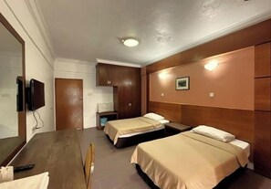 Une chambre d’hôtel avec une tête de lit en bois, deux lits simples, une table en bois, une télévision et une petite table de chevet avec une lampe.