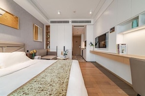 Una habitación de hotel moderna con una cama grande, un sofá, una mesita y una zona de kitchenette.