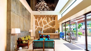 Un vestíbulo con una recepción, una pared de madera con diseños geométricos, una araña y una zona de estar con cojines.