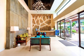 Una hall con reception, una parete in legno con motivi geometrici, un lampadario e un’area salotto con cuscini.