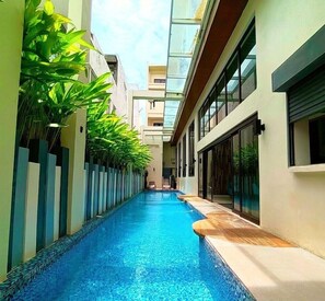 A narrow indoor swimming pool with clear blue water, flanked by vertical planters with green foliage, and modern architecture with large windows. - Ferra Premier Boracay by JG (Boracay Island)