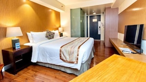 Una habitación de hotel con cama, mesita de noche, lámpara, televisor y un escritorio de madera.