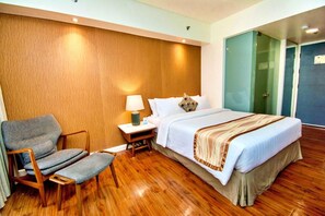 A hotel room with a bed, a chair, a nightstand, and a wooden floor. - Ferra Premier Boracay by JG (Boracay Island)