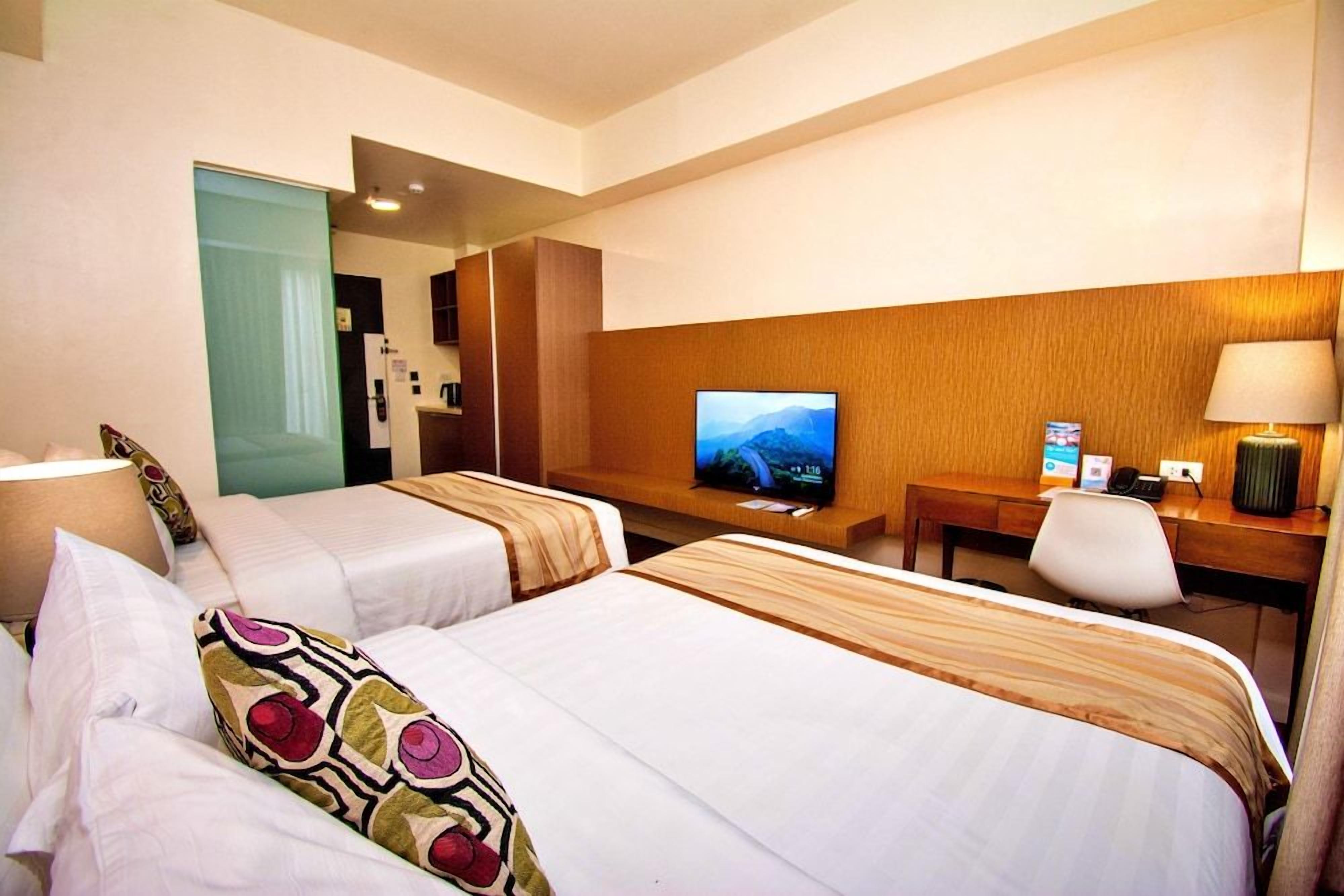 A hotel room with two beds, a desk with a television, and a chair.
