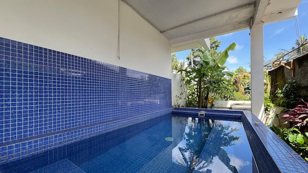 A swimming pool with blue tiles, surrounded by greenery and a clear sky. - Collection O Near Monkey Forest Formerly Hepiyuk Guest House (Ubud)