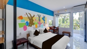 A hotel room with a large bed, a desk, a chair, and a balcony with a view of trees. - Collection O Near Monkey Forest Formerly Hepiyuk Guest House (Ubud)