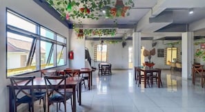 A spacious dining area with multiple tables and chairs, large windows, and a staircase leading to another level. - Collection O Near Monkey Forest Formerly Hepiyuk Guest House (Ubud)