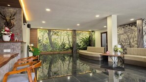 A lobby with a reflective floor, seating area, and a wall with a forest mural. - Hotel Anda (Jember)