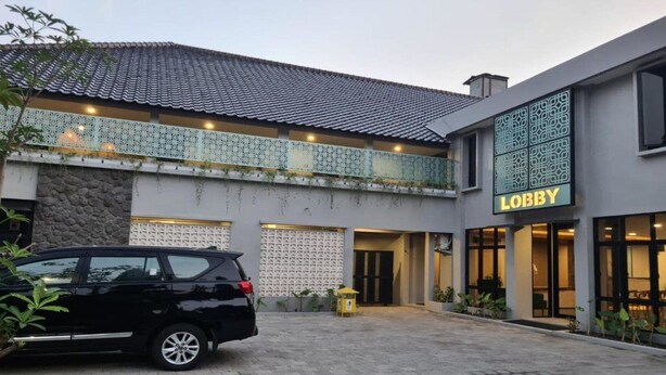 A building with a 'Lobby' sign, a car parked in front, and a stone wall. - Hotel Anda (Jember)