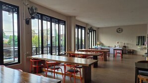 A spacious dining area with multiple tables and chairs, large windows, and a clock on the wall. - Hotel Anda (Jember)