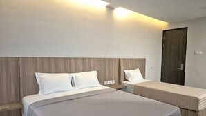 A hotel room with two beds, a wooden headboard, and a door. - Hotel Anda (Jember)
